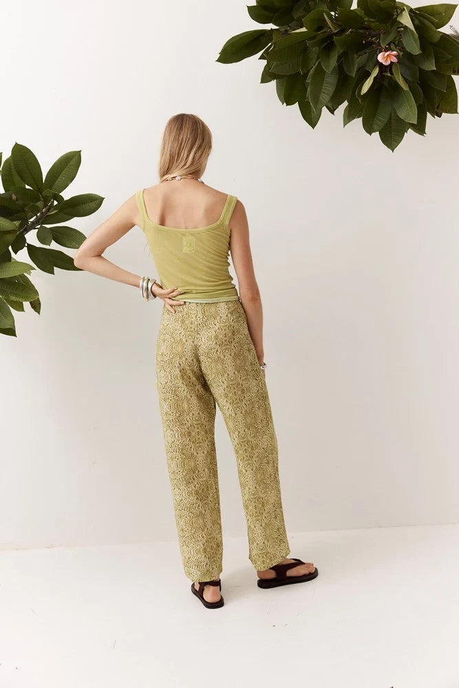 Back view of the Dorato printed wide-leg pants styled with a light green tank top and black sandals against a clean white studio background with leafy branches.