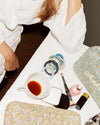 Green and silver glitter hair tie styled with coordinating woven hair ties, beauty products and a cup of tea on a white towel.