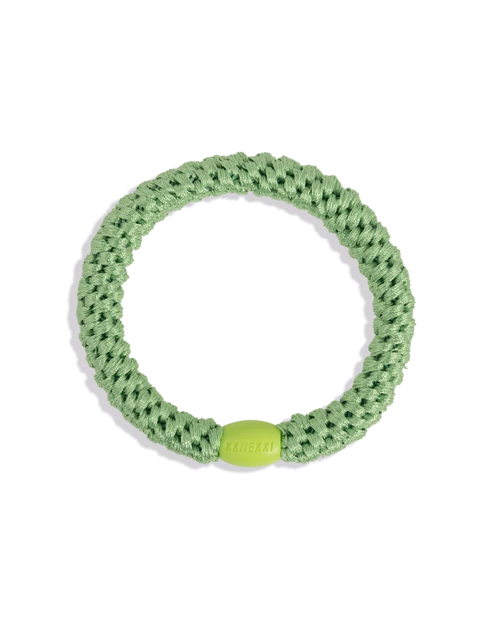 Grass green woven hair tie shown in a circular product view with a contrasting lime green bead on a clean background.