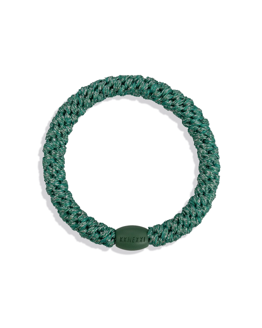 Teal-green glitter woven hair tie shown individually against a clean dark background, highlighting the circular shape, metallic texture and smooth branded bead.