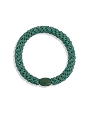 Teal-green glitter woven hair tie shown individually against a clean dark background, highlighting the circular shape, metallic texture and smooth branded bead.