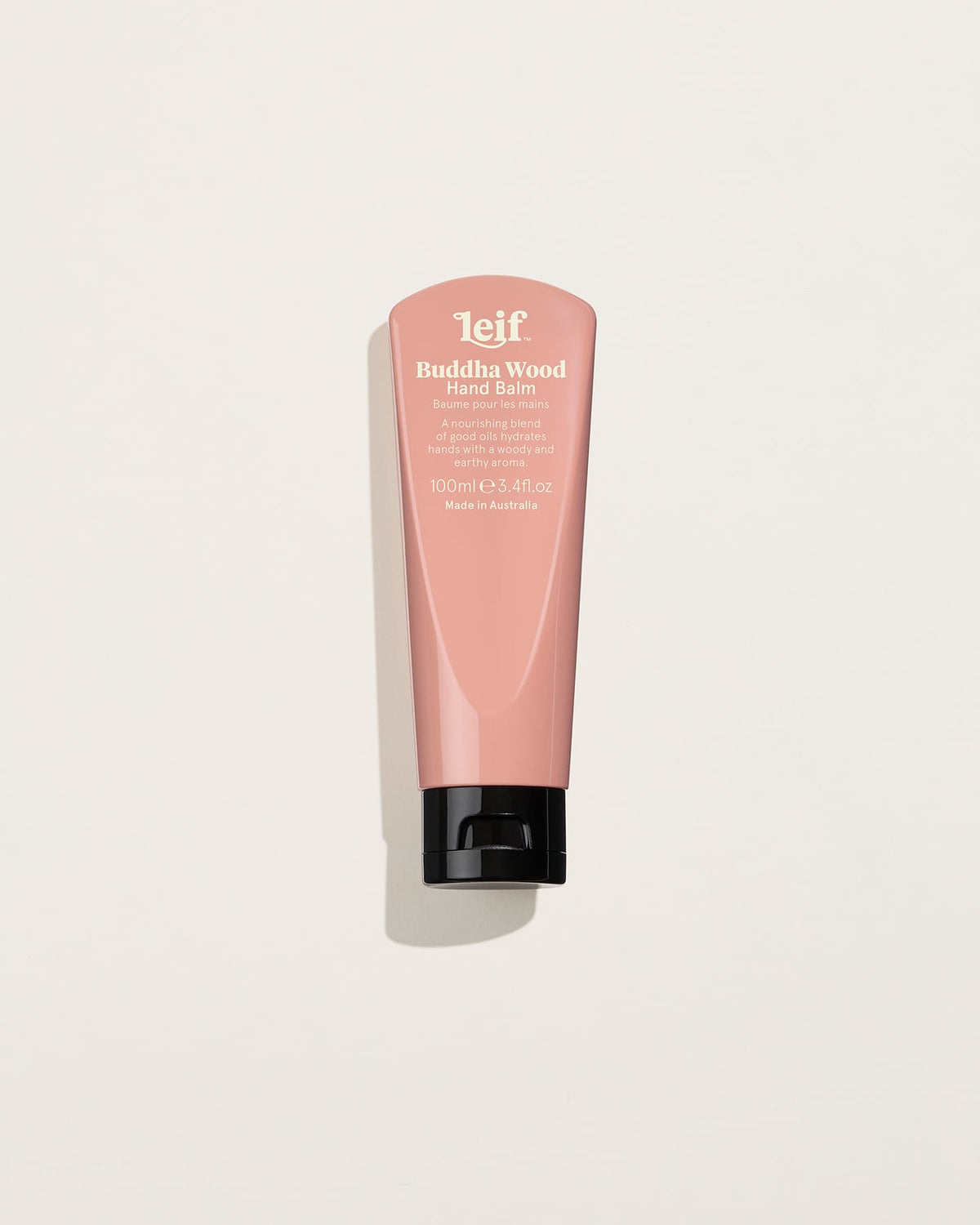 A pink 100ml hand balm tube with white lettering and a black flip-top cap is shown upright against a pale background with a soft shadow.