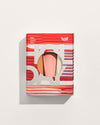 A red and white striped gift box with a circular cutout displaying a pink hand balm tube against a pale background.