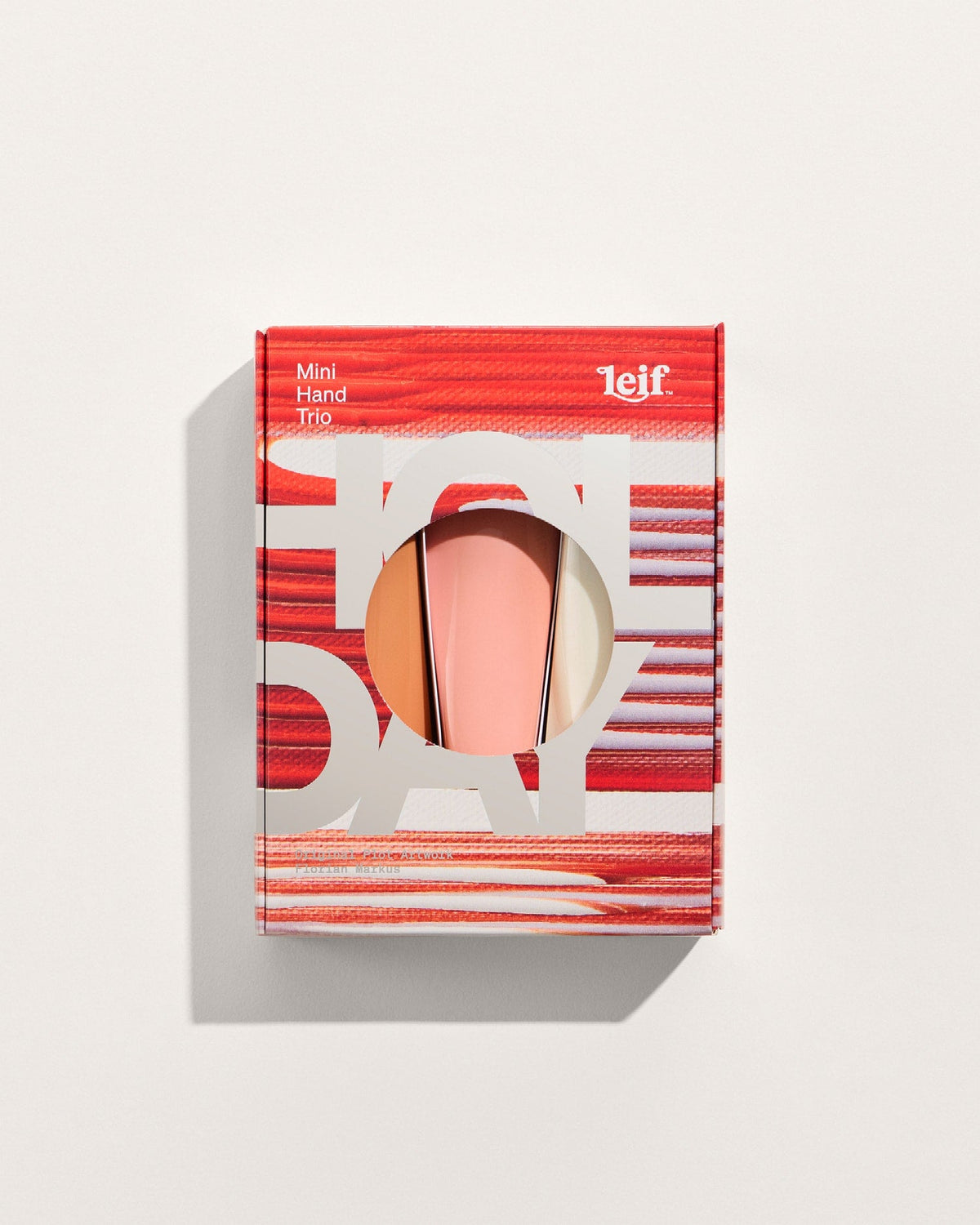 A red and white striped gift box with a circular cutout displaying a pink hand balm tube against a pale background.