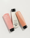 Three hand balm tubes in pink, cream and peach arranged diagonally against a light background.