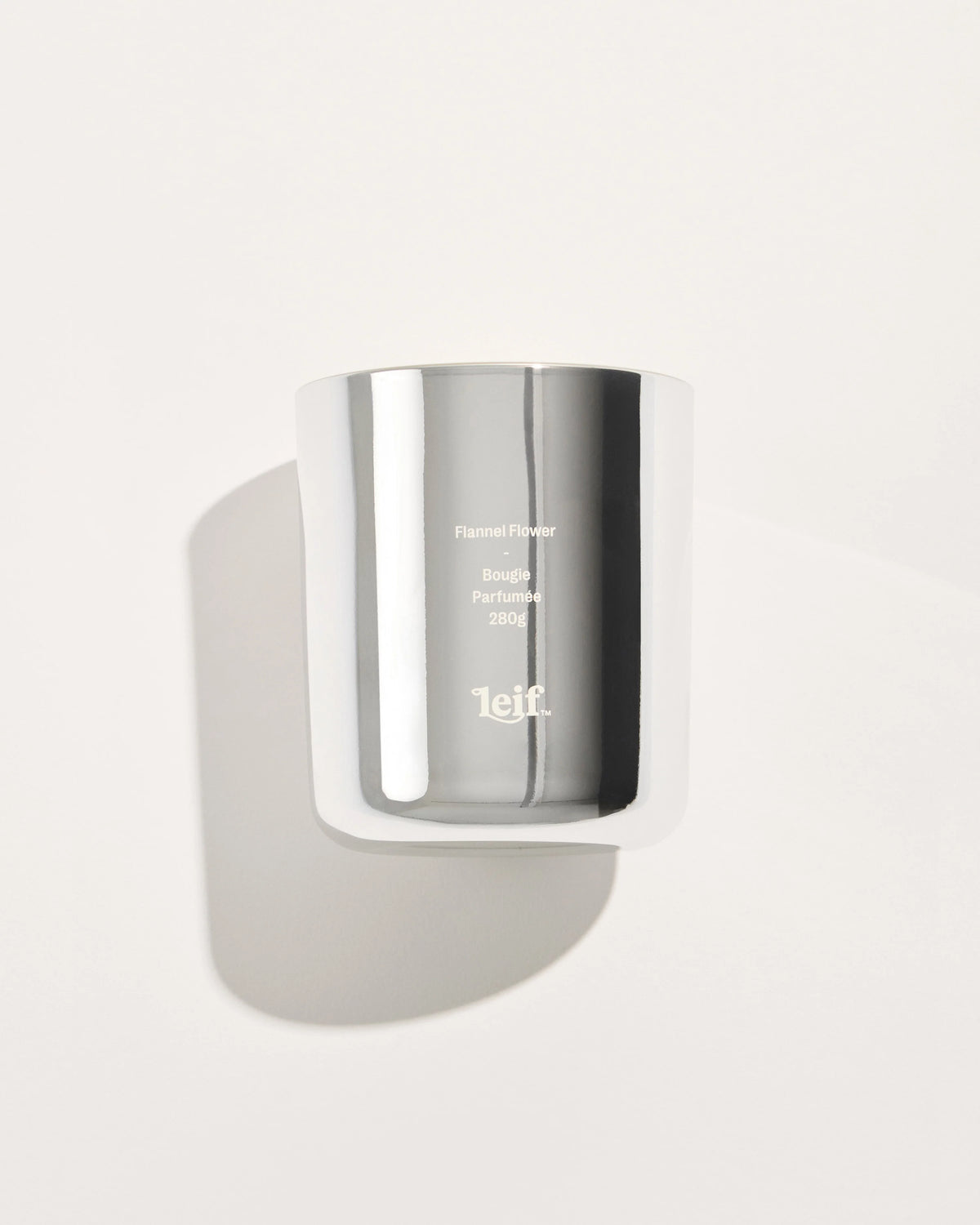 A chrome glass candle vessel with pale wax is shown from the front against a light background, displaying the Flannel Flower label.