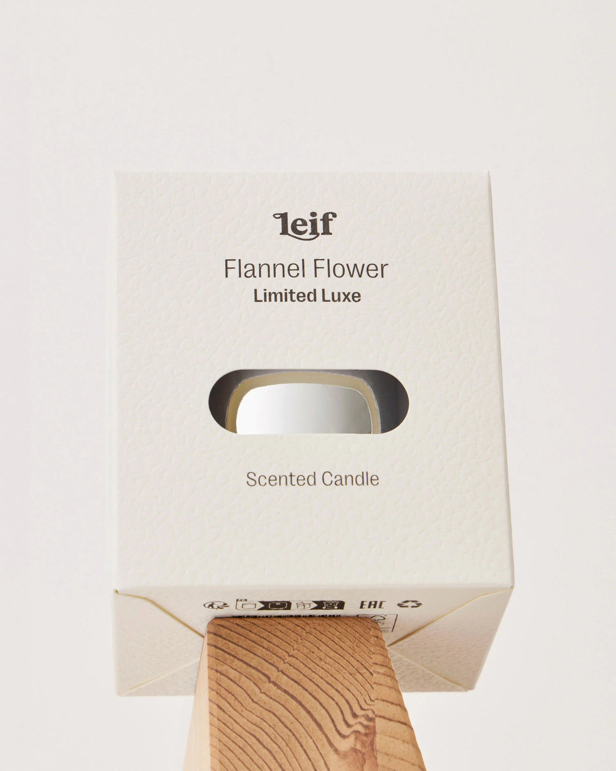 A close-up of the cream Flannel Flower Limited Luxe candle box shows its window revealing the reflective metallic vessel inside.