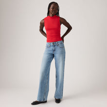Person wearing a red sleeveless top and blue jeans on a plain background