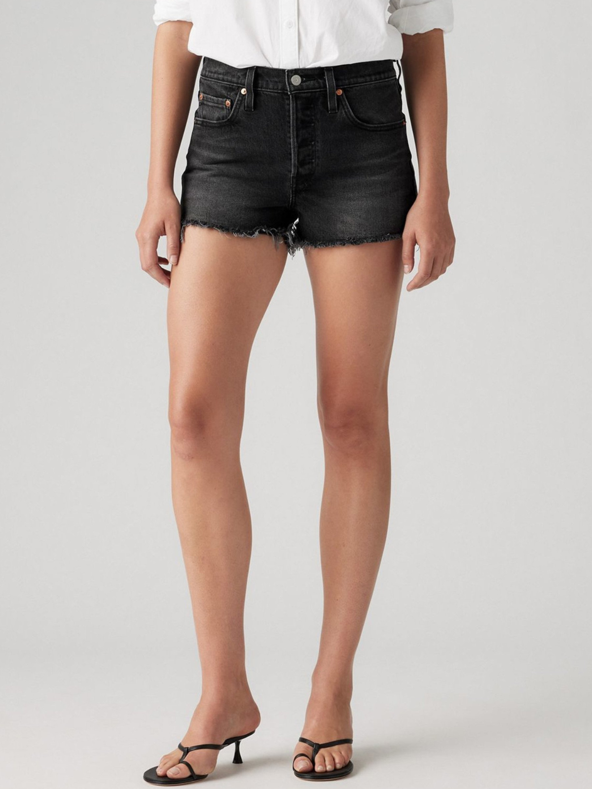 Close-up of black denim shorts showing the front pockets, button closure and frayed hems.