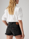 Close-up of the back of black denim shorts showing the waistband label, patch pockets and raw hems.