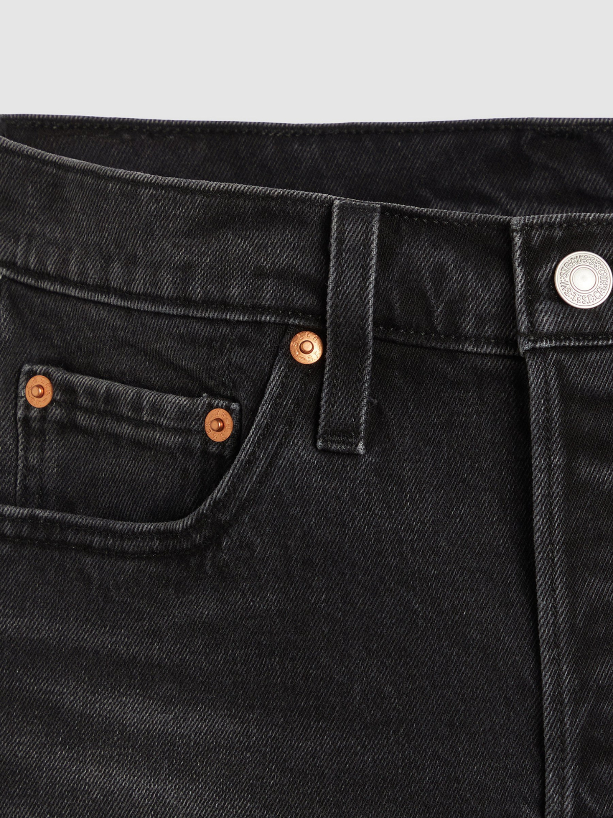 Close-up of black denim shorts showing the waistband, belt loop, metal button and copper-tone rivets.