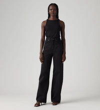 Model wearing Levi’s black high-rise wide-leg jeans with a black sleeveless top and strappy heels, showing the five-pocket design and full-length silhouette, front view