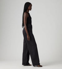 Model wearing Levi’s black high-rise wide-leg jeans with a black sleeveless top and strappy heels, showing the fitted waist and wide-leg profile, side view