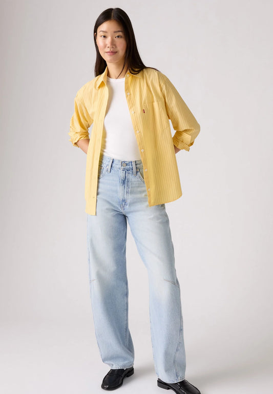 Front view of the light-wash jeans styled with a yellow striped shirt and black loafers, showing the loose barrel-leg silhouette.