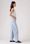 Side view of the light-wash jeans worn with a white tank top, showing the curved barrel-leg silhouette and back pocket.