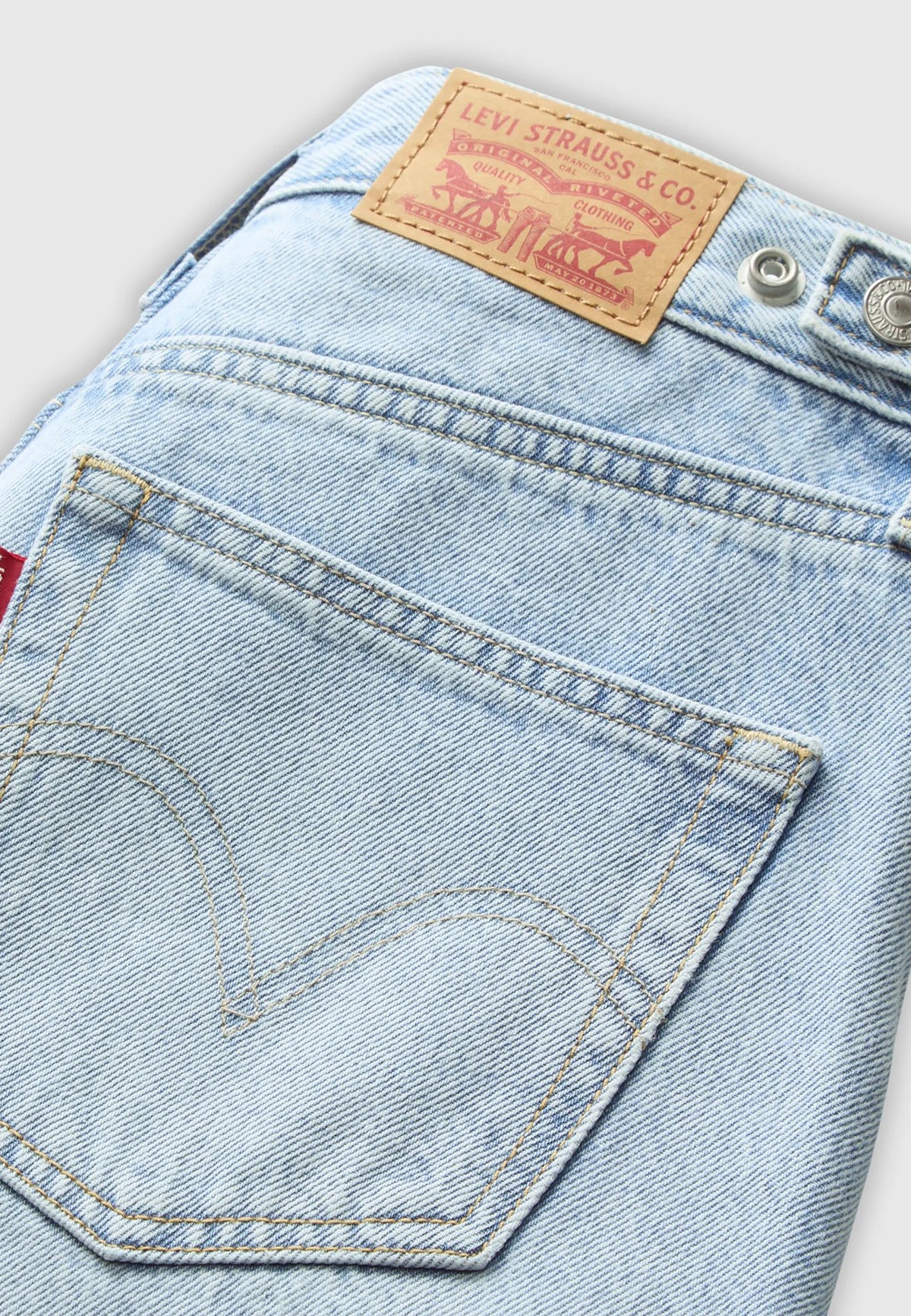 Close-up of the light-wash jeans showing the back pocket stitching, waistband patch and metal buttons.