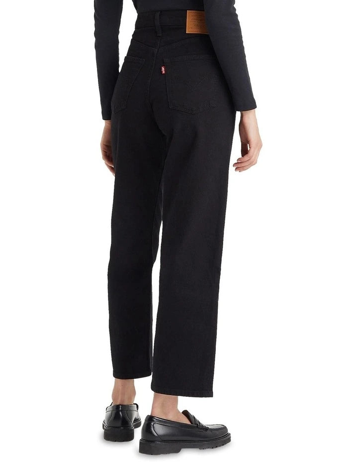 A model wears the black ankle-length jeans in a rear studio view showing the back patch pockets and straight-leg fit.

