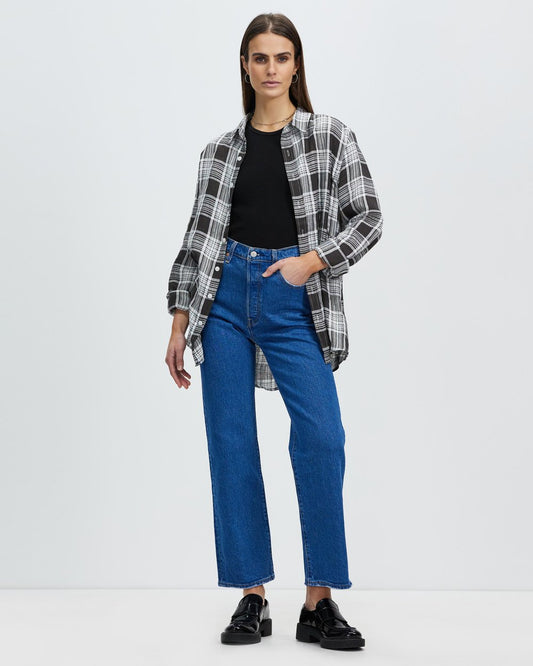 Woman wearing a plaid shirt, black top, and blue jeans on a white background