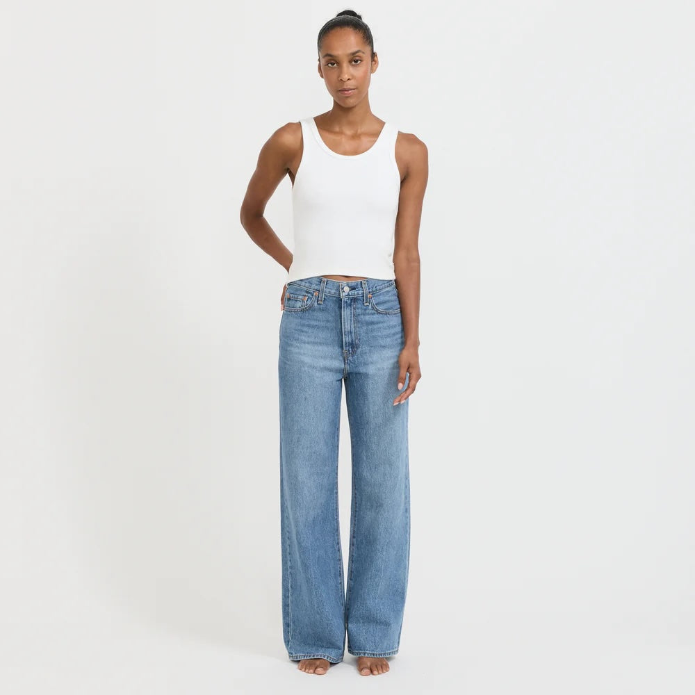 Woman wearing a white tank top and blue jeans on a light gray background
