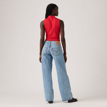 Person wearing a red sleeveless top and light blue jeans on a plain background