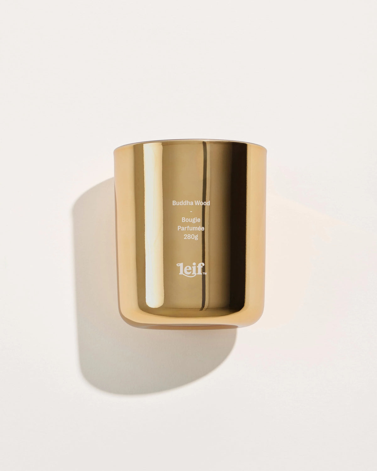 A gold reflective glass candle vessel with a Buddha Wood label is photographed from the front against a pale background.