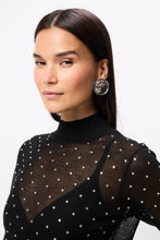 Woman wearing a black top with sheer polka dot overlay against a white background