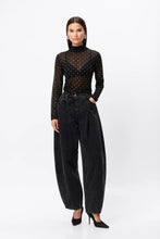 Woman wearing a black polka dot top and black jeans on a white background