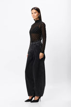 Woman wearing a black polka dot top and black high-waisted pants on a white background