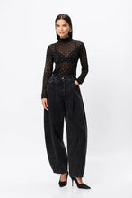 Woman wearing a black sheer top with polka dots and high-waisted black jeans on a white background