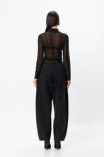 Woman wearing a black polka dot blouse and black pants on a white background
