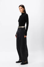 Person wearing a black turtleneck and high-waisted black pants on a white background