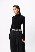 Woman wearing a black turtleneck and wide-leg jeans with a patterned belt on a white background