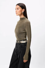 Woman wearing a green turtleneck sweater and black pants on a white background