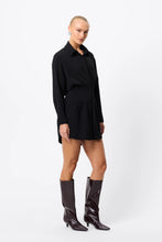 A model wears the black long-sleeve mini dress in an angled front view with knee-high boots.
