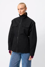 A model wears the Mossman Hamilton Anorak in black with blue wide-leg jeans in an angled front studio view.
