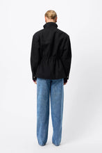 A model wears the black anorak in a back studio view showing the gathered waist and high collar.
