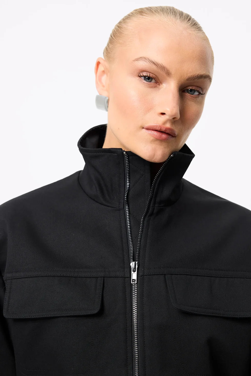 A close-up shows the high collar, front zip and flap chest pockets on the black anorak.
