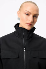A close-up shows the high collar, front zip and flap chest pockets on the black anorak.
