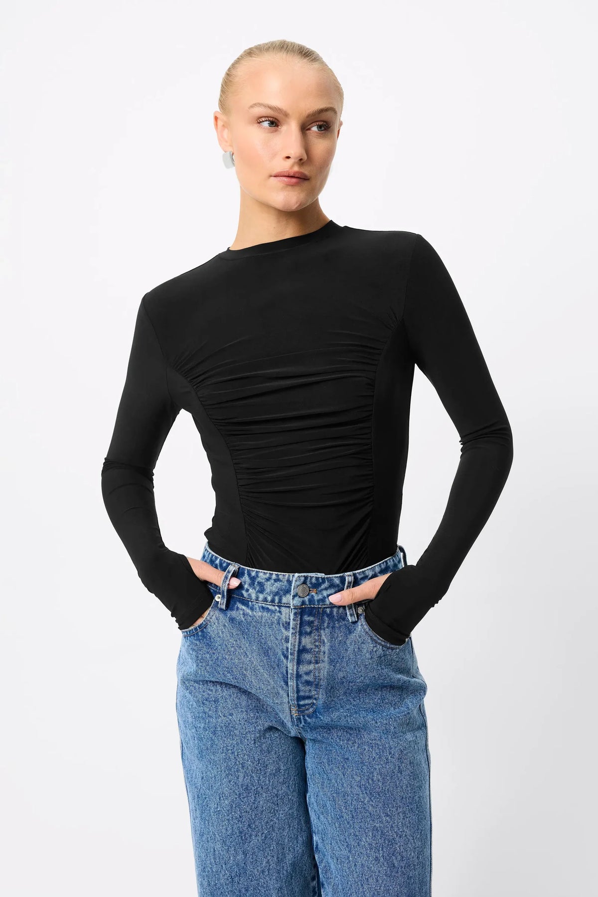 A model wearing a black long-sleeve top with ruching and a boat neckline, paired with blue jeans, against a light gray background.