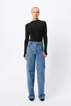A model wears the black long-sleeve top with blue wide-leg jeans in a full-length front studio view.
