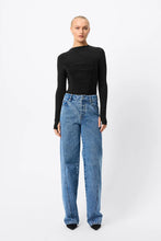 A model wears the black long-sleeve top with blue wide-leg jeans in a full-length front studio view.
