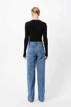 A model wears the fitted black long-sleeve top in a back studio view with blue jeans.
