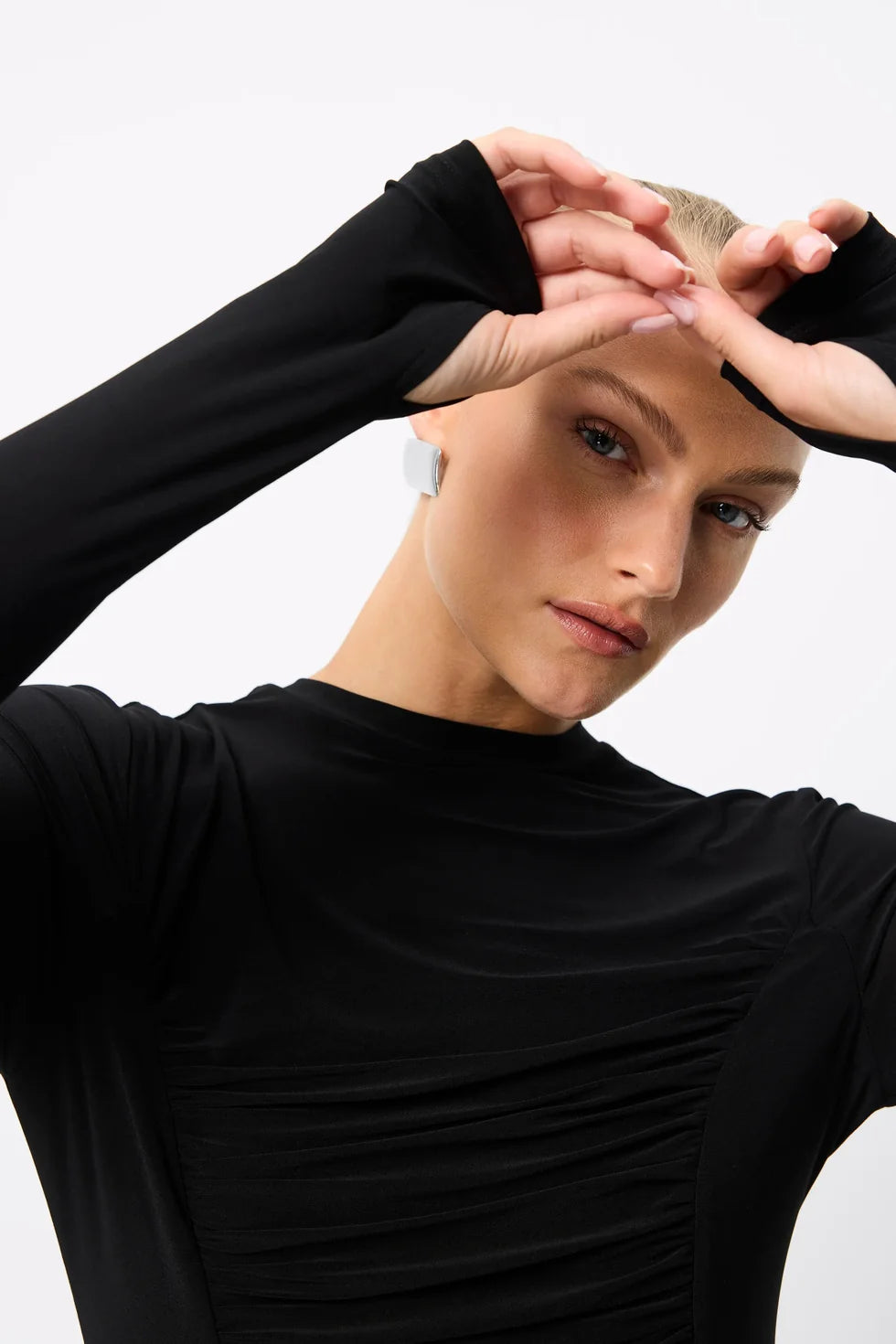 A close-up shows the high neckline, ruched front and extended sleeves with thumbholes on the black top.
