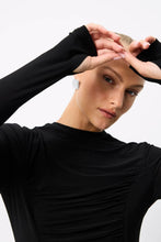 A close-up shows the high neckline, ruched front and extended sleeves with thumbholes on the black top.
