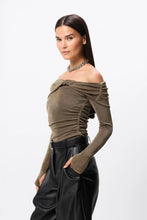 woman standing on her side with an off the shoulder long sleeve top on looking at the camera