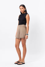 Woman wearing a black sleeveless top and beige shorts on a white background