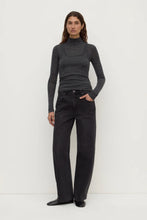 Woman wearing a gray turtleneck and black jeans on a white background