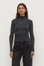Woman wearing a dark gray turtleneck sweater and black pants on a white background