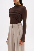 Three-quarter view highlighting the draped front detail, long sleeves and slim fit.