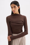 Model posing in the chocolate top with arms crossed, highlighting the raised neckline and extended sleeves.